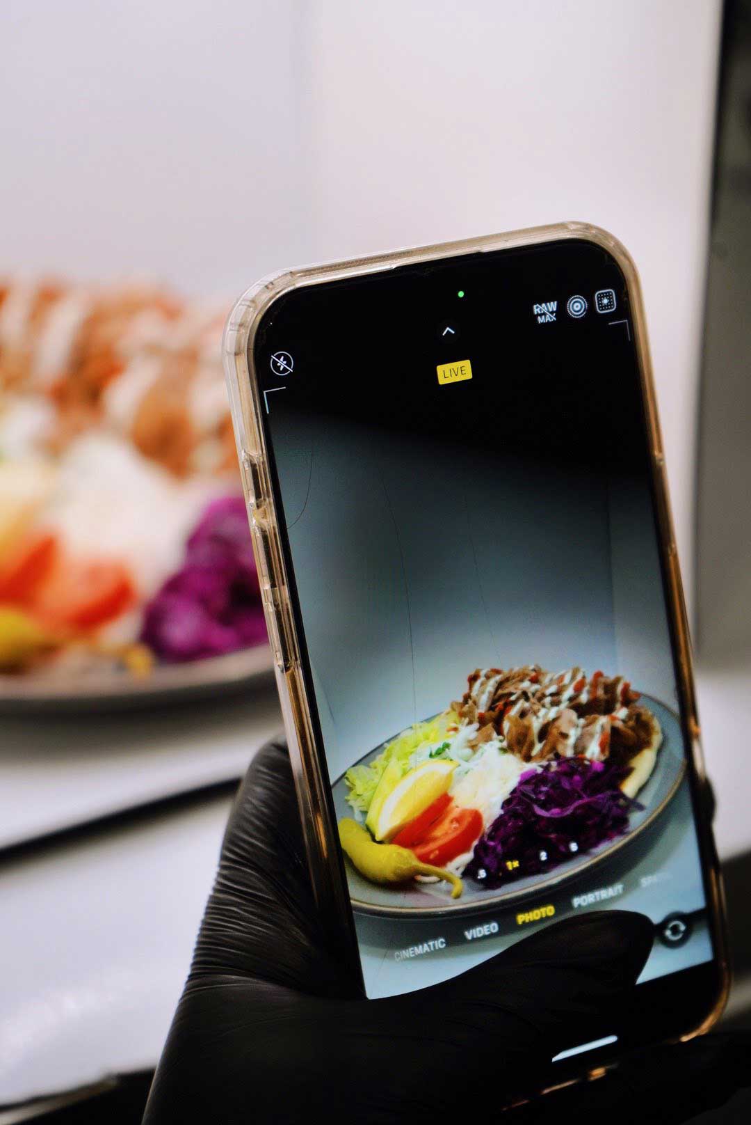 A smartphone takes a picture of the Sensation Takeaway plate, including doner, cabbage, and rice.